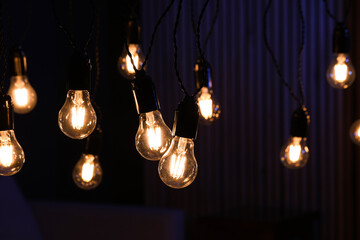 Glowing light bulbs hanging indoors, closeup view