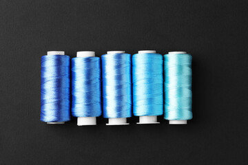 Spools of colorful sewing threads on black background, flat lay