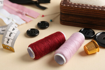 Different sewing supplies on beige background, closeup