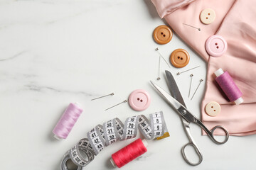 Different sewing supplies on white marble table, flat lay. Space for text