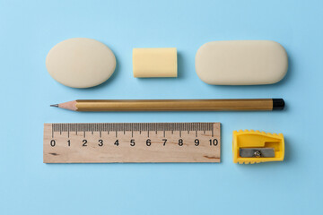 Erasers and other stationery on light blue background, flat lay