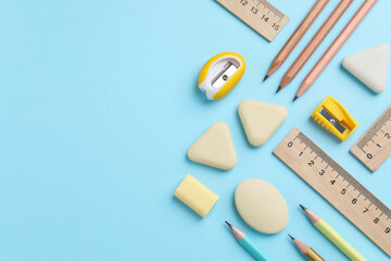 Erasers and other stationery on light blue background, flat lay. Space for text