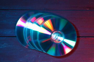 Shiny compact discs on wooden background, top view