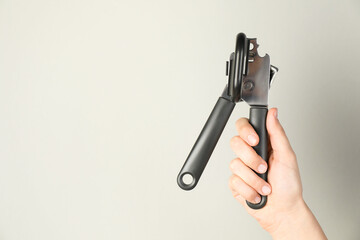 Woman holding can opener against light background, closeup. Space for text