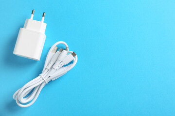 USB power adapter and triple charge cable on light blue background, flat lay. Space for text
