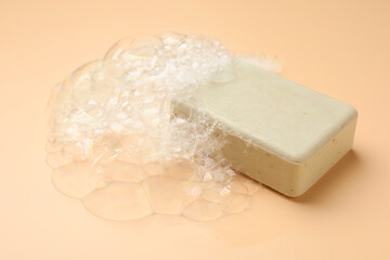 Soap bar with foam on peach background, closeup