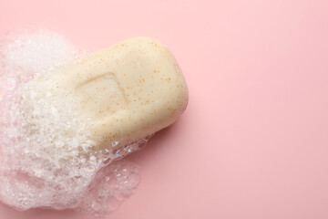 Fototapeta premium Soap bar with foam on light pink background, top view. Space for text