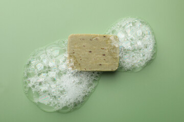 Soap bar with foam on green background, top view