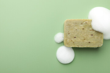 Soap bar with foam on green background, top view. Space for text