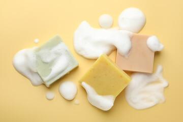 Soap bars with foam on yellow background, flat lay