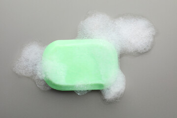 Soap bar with foam on grey background, top view