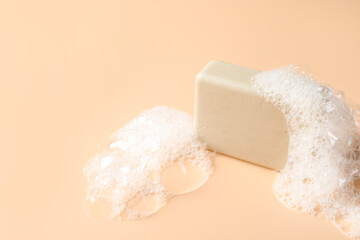 Soap bar with foam on beige background, closeup. Space for text