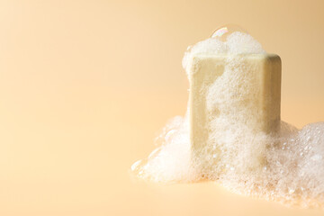 Soap bar with foam on beige background, closeup. Space for text