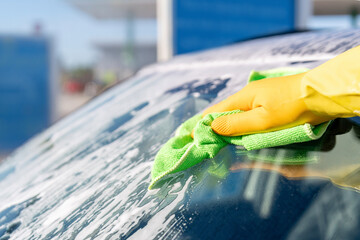 Cleaning windshield at service station  using  microfiber cloth on bright sunny day