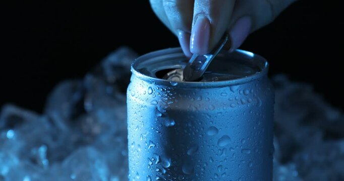 Woman opening can of refreshing drink in blue light on black background, closeup