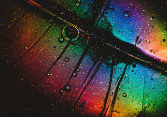 Macro abstract texture with vibrant iridescent rainbow colour spectrum and scattered tiny bubbles on a dark grainy background