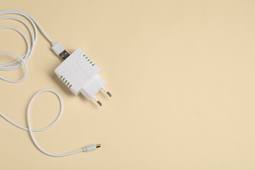 USB power adapter with charge cable on beige background, top view. Space for text