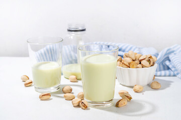Vegan alternative Pistachio Milk,  Healthy vegetarian drink. Two glass with non-dairy milk beverage, on white kitchen table with pistachio nuts, copy space