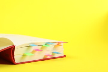 Book with colorful tabs on yellow background, closeup. Space for text