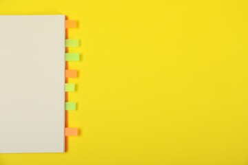 Book with colorful tabs on yellow background, top view. Space for text