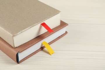 Books with ribbon bookmarks on light wooden table, closeup. Space for text