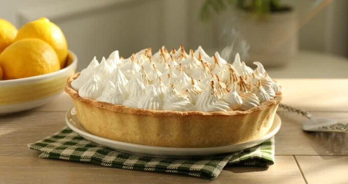 Toasting meringue on lemon pie with kitchen torch at wooden table, closeup