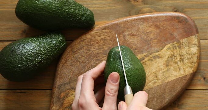Woman cutting ripe avocado at wooden table, top view