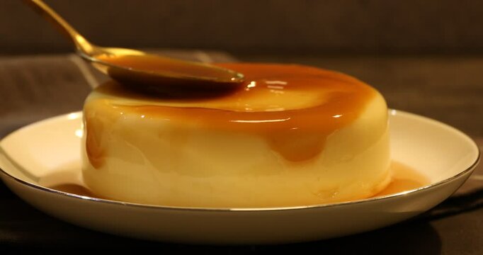 Spreading caramel sauce onto delicious pudding at table, closeup