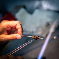Close-up of artisan crafting glass bead with flame. 