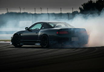 Black sports car drifting on race track with smoke trail