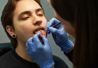 Professional piercer performing lip piercing on young punk with gloves and tools
