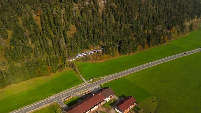 Drone shot of a regional train nearing Bayrischzell station during fall, framed by colorful autumn trees in Bavaria, Germany. A serene view of nature and railways in perfect harmony
