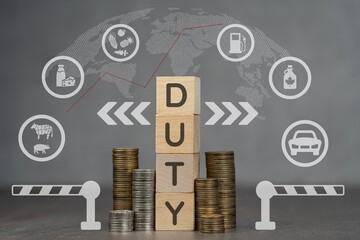 Drewniane kostki z napisem DUTY, obok sterta monet . Koncepcja wzrostu ceł.  © siwyk