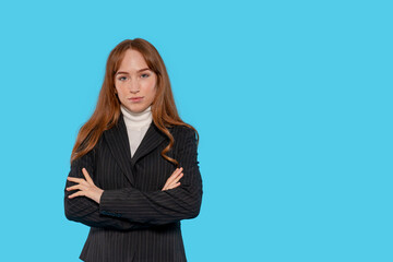 Confident young woman in black pinstripe suit with arms crossed against a bright blue background...