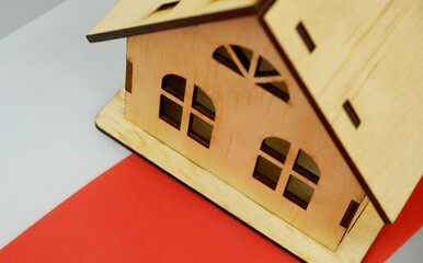 Wooden house model and Polish flag on gray background. Real estate in Poland concept.