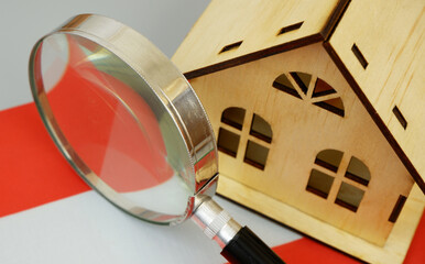 Wooden house model, magnifying glass and Austrian flag on gray background. Find real estate in...