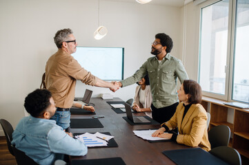 Two businessmen shake hands at the end of a successful business meeting. A diverse group of...