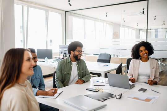 A business team enjoys a lighthearted moment during a meeting in a bright office. The diverse group fosters a collaborative and friendly work atmosphere