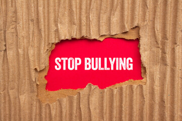 Stop bullying message written on ripped torn cardboard paper on red background. Conceptual stop...