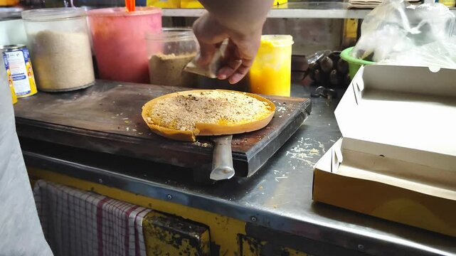 Male chef sprinkles peanut powder and chocolate powder topping on terang bulan bread or sweet martabak