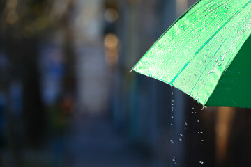 Open green umbrella under pouring rain outdoors, closeup. Space for text