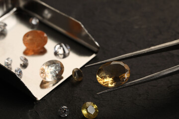Tweezers with beautiful gemstones on black table, selective focus