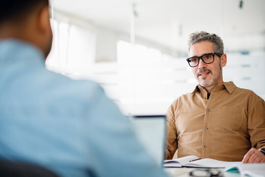 A senior executive engaged in a one-on-one discussion in a bright, modern office. His focused expression and open body language reflect leadership, mentorship, and strategic thinking.
