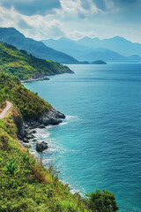 Obraz premium Stunning coastal view of rocky shore and lush greenery against blue mountains