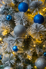 Christmas tree branch with gray and blue ball and blur background. Christmas tree decorated with lights that glow yellow. Close-up of Fully Decorated Christmas tree.

