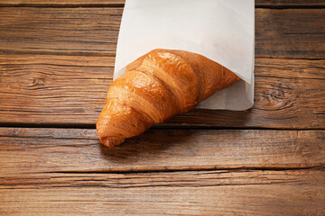 Paper bag and fresh croissant on wooden table, closeup