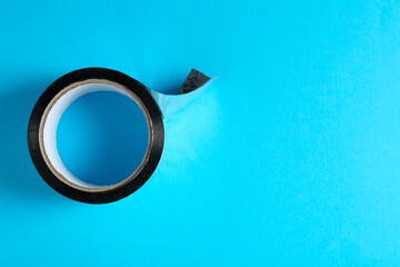 Roll of black adhesive tape on light blue background, top view. Space for text