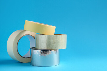 Rolls of different adhesive tapes on light blue background, space for text