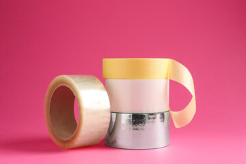 Rolls of different adhesive tapes on pink background