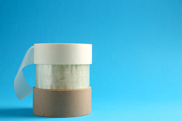 Rolls of different adhesive tapes on light blue background, space for text